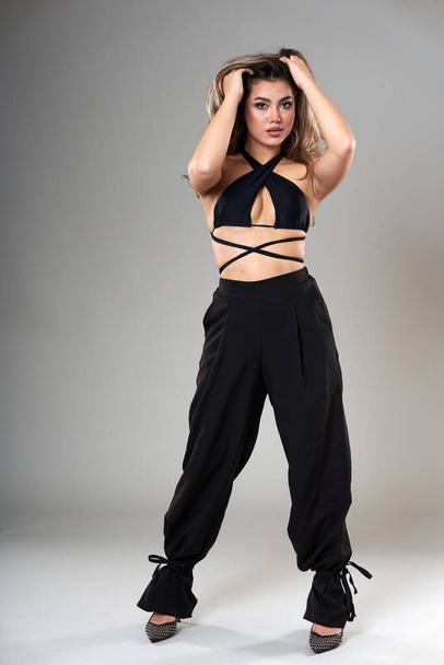 Young beautiful fashionable model in trendy black top and trousers studio shot on gray background - Foto, Imagem