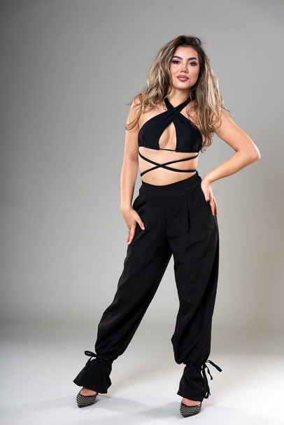 Young beautiful fashionable model in trendy black top and trousers studio shot on gray background - Foto, immagini