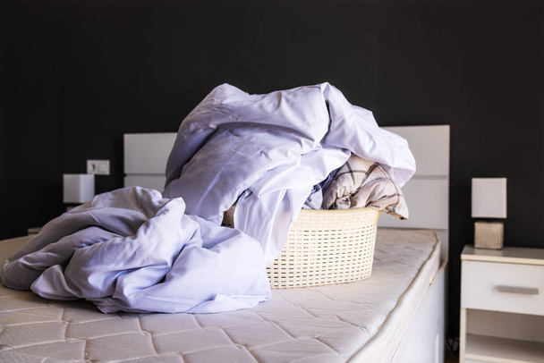 Az ágyon egy nagy halom koszos ágyneműt gyűjtenek egy mosdókagylóba, hogy kimossák. A házi feladat fogalma, takarítás a lakásban, stúdió, lakás foglalás. Mosodai fogalom, folyékony ágynemű mosószer - Fotó, kép