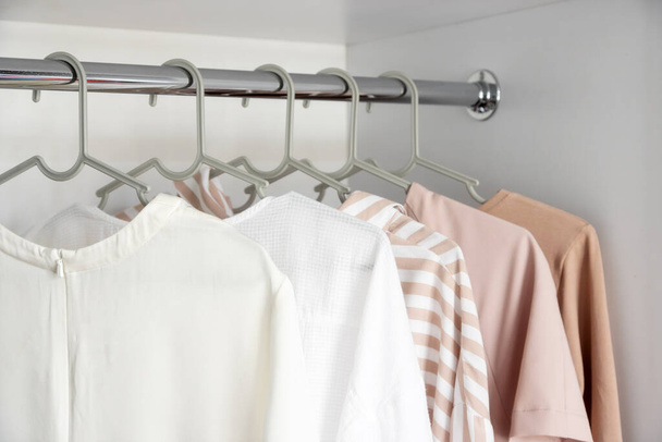 Colored clothes hang on a hanger in a home closet or store. Shirts, blouses, jackets, different colors. The concept of a clothing store, the work of a stylist in the selection of clothes - Foto, Bild
