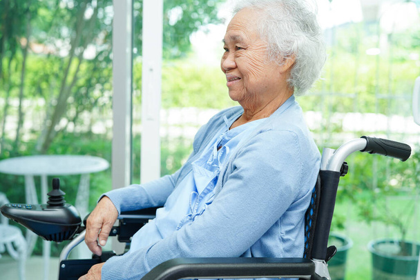 Asian elderly woman disability patient sitting on electric wheelchair in park, medical concept. - Fotó, kép