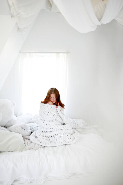 Woman covered with a thick warm blanket on the bed. White interior. Cold winter. Saving electricity and gas. Depression, insomnia. - Foto, afbeelding