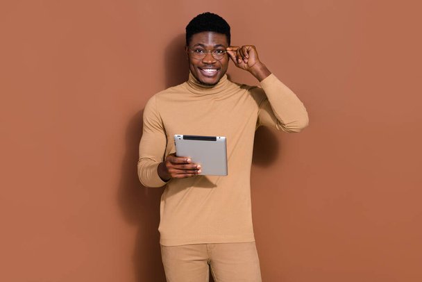 Portrait of attractive cheerful guy holding using device web site order touching specs isolated over brown color background. - Foto, imagen