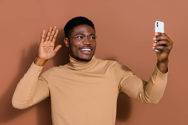 Portrait of handsome trendy cheerful guy blogger taking selfie waving greetings isolated over brown color background. - Fotoğraf, Görsel