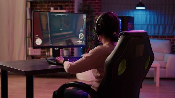 Gamer girl using pc gaming setup relaxing playing multiplayer online action game talking using headset in tournament. Woman streaming first person shooter while explaining gameplay to subscribers. - 写真・画像