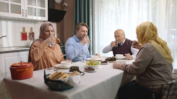 Счастливая мусульманская семья ужинает вместе на кухне. Мусульманская турецкая семья прерывает свой пост за ифтаровым столом. Ифтар - вечерняя трапеза, за которой мусульмане  - Фото, изображение