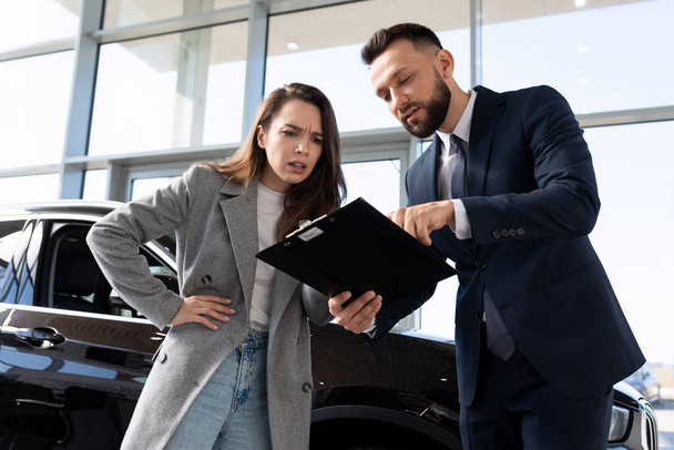 jonge vrouw koper in een auto-dealer begrijpt de nuances van het contract bij het kopen van een nieuwe auto. - Foto, afbeelding
