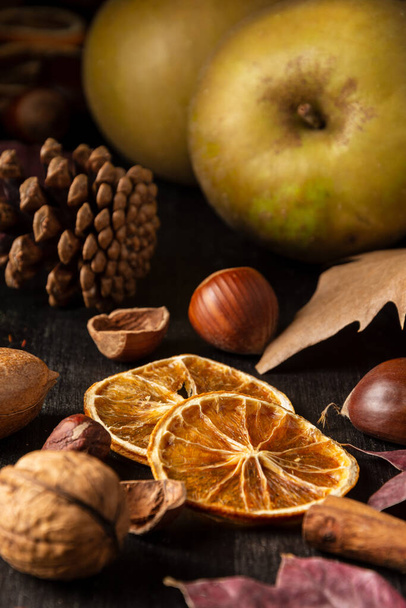 Close-up of dried orange slices on wooden table with nuts, cinnamon, apples and autumn leaves, selective focus, vertical - Фото, зображення