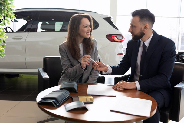 mužský manažer prodává nové auto mladé ženě v prodejně aut. - Fotografie, Obrázek