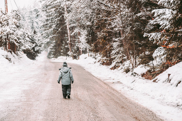 Een jongensjasje loopt door een besneeuwd bos. Wandelen in de frisse lucht op een winterdag. Levensstijl concept. - Foto, afbeelding