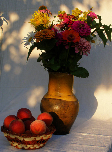 Boeket zomerbloemen in een kleivaas op een lichte stofondergrond. Perziken die in een diepe plaat naast elkaar staan - Foto, afbeelding
