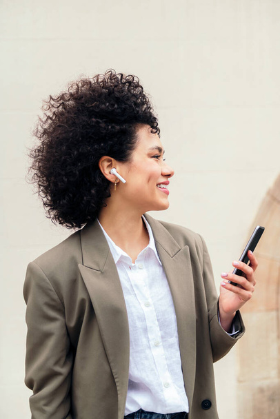 young business woman with wireless earphones smiles happy talking hands free on her phone, concept of entrepreneurship and technology of communication, copy space for text - Фото, зображення