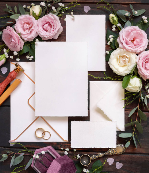 Cards and envelope between pink and cream roses on brown wood top view,  wedding mockup. Romantic scene with cards, envelope, rings and pastel flowers flat lay. Valentines, Spring or Mothers day concept - Фото, зображення