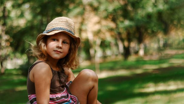 Tyttö olkihatussa ulkona. Söpön tytön muotokuva 5-vuotias. Lapsi istuu puistossa. Kopioi tila. - Valokuva, kuva