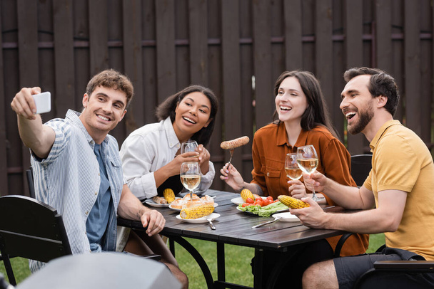 cheerful multiethnic friends taking selfie during bbq party in backyard   - Photo, Image