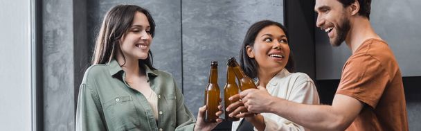 veselí multietničtí přátelé drží láhve piva a cinkání v kuchyni, banner - Fotografie, Obrázek