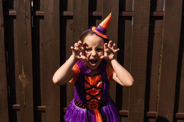 Mädchen im Halloween-Kostüm blickt mit wütender Fratze in die Kamera und zeigt beängstigende Gesten - Foto, Bild