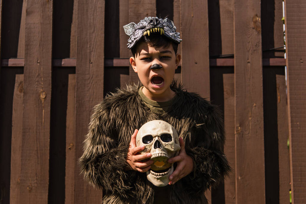 Asijské dítě v vlkodlačí kostým vrčení a držení lebky při pohledu na kameru - Fotografie, Obrázek
