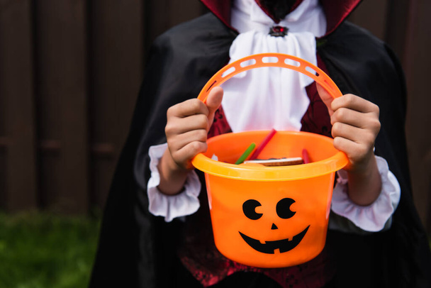 cropped view of boy in halloween costume holding trick or treat bucket with sweets - Photo, Image