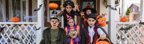 chicas mostrando gestos de miedo cerca de amigos multiétnicos en trajes de Halloween, pancarta - Foto, Imagen