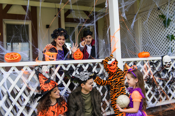 Rotujenvälinen lapset halloween puvut puhuvat lähellä sisustus talon  - Valokuva, kuva