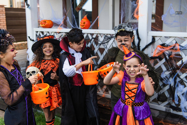 Межрасовые дети в костюмах на Хэллоуин держат ведра и играют на открытом воздухе  - Фото, изображение