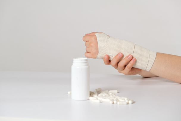 Une main avec un bandage élastique et un bocal de calcium ou de comprimés de chondroïtine. Traitement des fractures, des entorses et des maladies articulaires. - Photo, image