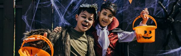 Pozytywne azjatyckie dzieci w halloween kostiumy trzymając wiadra i patrząc na kamery na zewnątrz, sztandar  - Zdjęcie, obraz