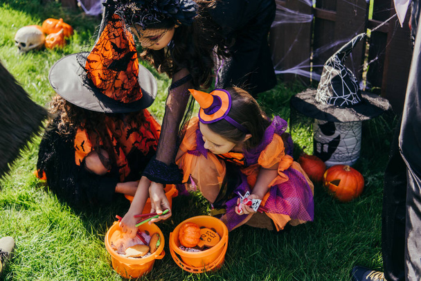 Preteen girls in halloween costumes taking candies from buckets in backyard  - Фото, зображення