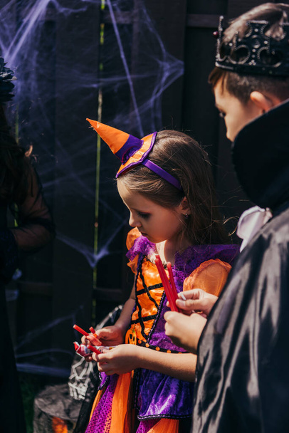 Multiethnic children in festive costumes holding candies during halloween celebration  - Фото, изображение