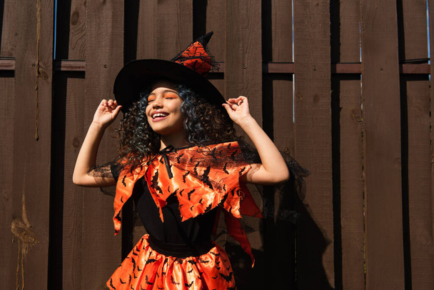 Положительный ребенок держит шляпу ведьмы во время празднования Хэллоуина на открытом воздухе  - Фото, изображение
