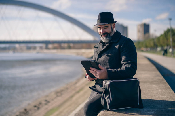 Бізнесмен сидить на вулиці в місті і використовує цифровий планшет
. - Фото, зображення