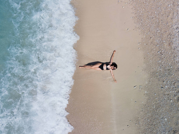 vista aérea de la mujer en traje de baño negro tomar el sol en la playa de arena de la orilla del mar - Foto, Imagen