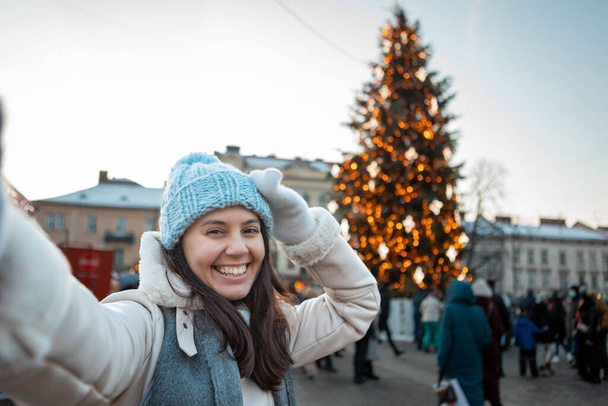 beautiful smiling women taking selfie picture at city square christmas tree on background copy space - Fotó, kép