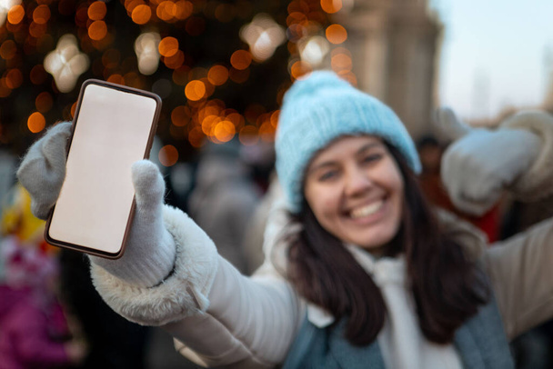 χαμογελαστή ευτυχισμένη γυναίκα στα Χριστούγεννα πόλη δίκαιη κρατώντας τηλέφωνο με λευκό οθόνη αντίγραφο χώρου - Φωτογραφία, εικόνα