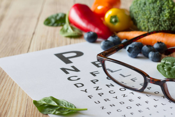 Food for eyes health, colorful vegetables and fruits, rich in lutein, eyeglasses and eye test chart on wooden background, concept  - Foto, Bild