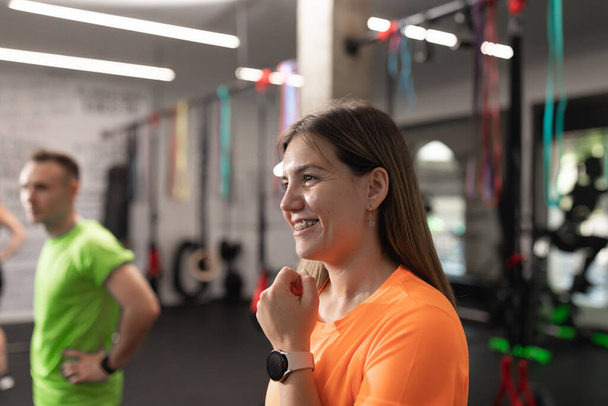 Portret uczennicy uśmiechającej się i umieszczającej zegarek podczas odpoczynku podczas treningu na siłowni - Zdjęcie, obraz