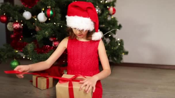 Cute girl opening gifts, present box near christmas tree in the morning at home. Merry Christmas and Happy Holidays. - Footage, Video