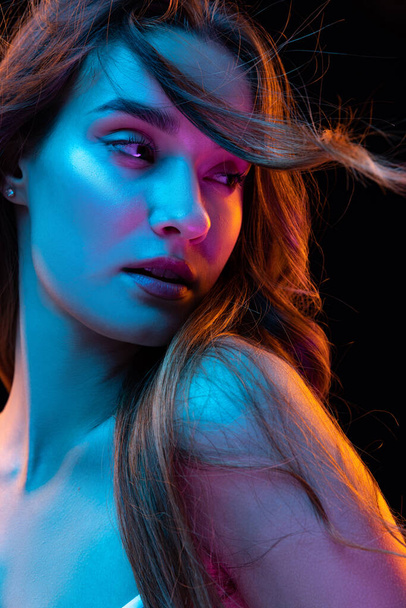 Charming look. Young beautiful girl with curly long hair isolated over dark blackground in neon light. Looks happy and relaxed. Health, beauty, fashion and ad concept. Closeup - Foto, immagini