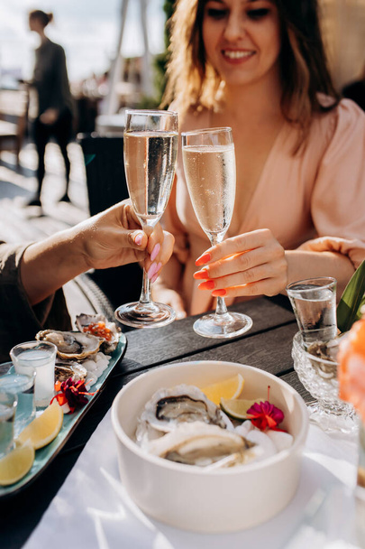Two Women friends eating fresh oysters and drinking chilled prosecco wine on the summer sunset in restaurant. Seafood delicacies - Foto, immagini