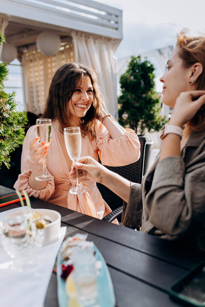 Две подруги едят свежие устрицы и пьют охлажденное вино Просекко на летнем закате в ресторане. Морепродукты деликатесы - Фото, изображение