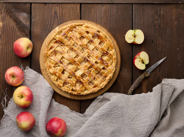 Круглий запечений яблучний пиріг на коричневому дерев'яному столі, вид зверху
 - Фото, зображення