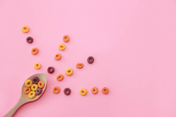 suché dětské sladké snídaně barevné kroužky v dřevěné lžíci na růžovém pozadí - Fotografie, Obrázek