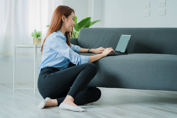Азиатка работает дома с ноутбуком сидя на диване онлайн рабочая концепция - Фото, изображение