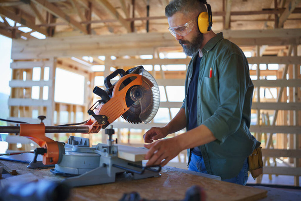 Construction worker working with eletric saw inside a wooden construction of house, diy eco-friendly homes concept. - Φωτογραφία, εικόνα