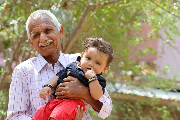 Indianin Zdjęcie dziadka i uroczego dziecka na zewnątrz. Azjatycki starzec trzymający wnuka w ramionach. Pali Rajasthan, Indie - Zdjęcie, obraz