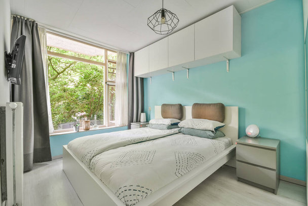 Cama moderna con colchón cómodo y almohadas suaves ubicadas cerca de la mesita de noche en un amplio dormitorio - Foto, imagen
