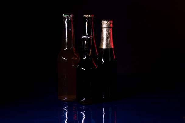 Silhouetten von vier Bierflaschen auf schwarzem Hintergrund, auf einer blau glänzenden Oberfläche. - Foto, Bild