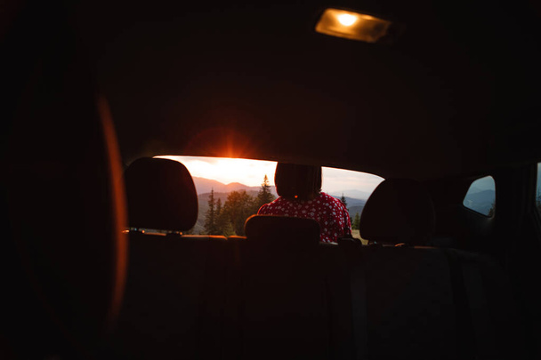 a woman sits in the trunk of a car with a view of the sunset in the carpathians mountains - Foto, Imagem