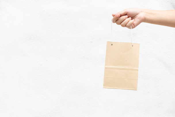 Hand of business woman hold brown paper shopping bag on white concrete background - Fotoğraf, Görsel